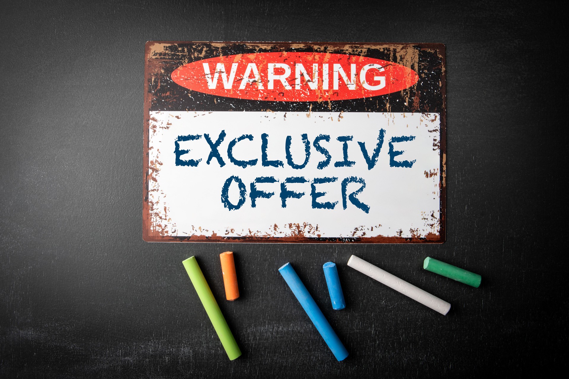 Offre exclusive. Panneau d’avertissement en métal et morceaux de craie colorés sur un fond de tableau noir sombre